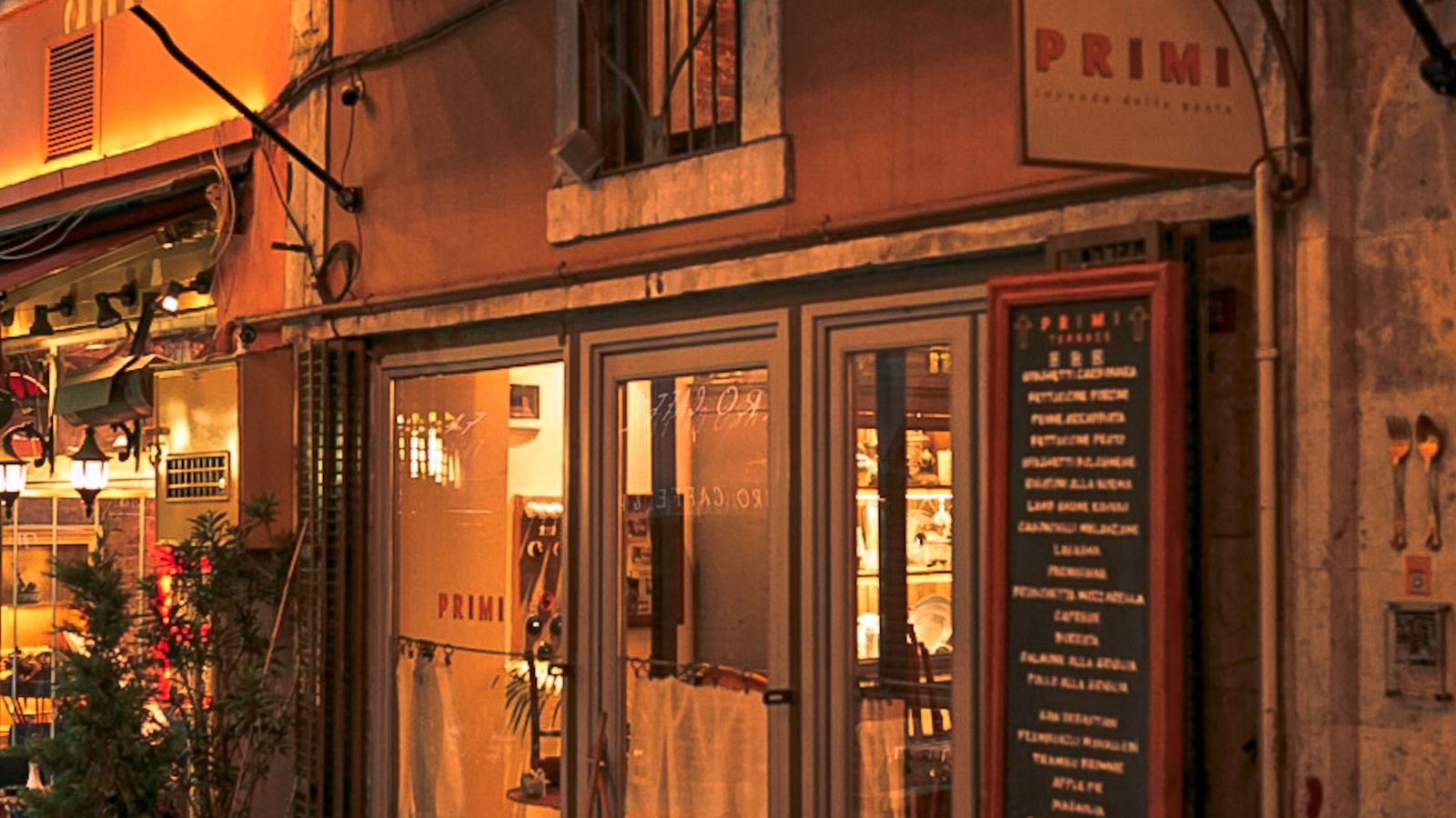 A warmly lit neighborhood restaurant storefront at night with a chalkboard menu outside